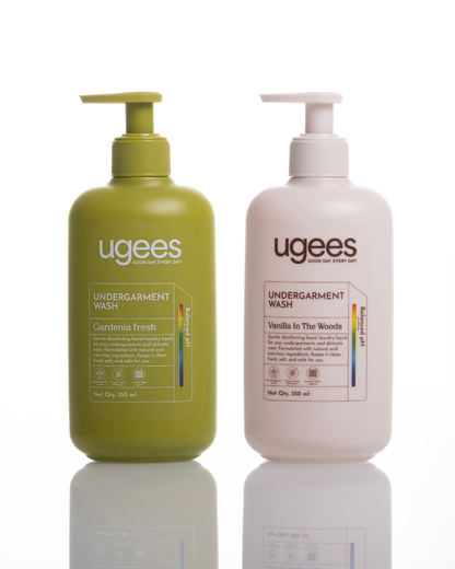 Two Ugees Undergarment Wash pump bottles on a white reflective background. The left bottle is olive green with a matching pump and reads &
