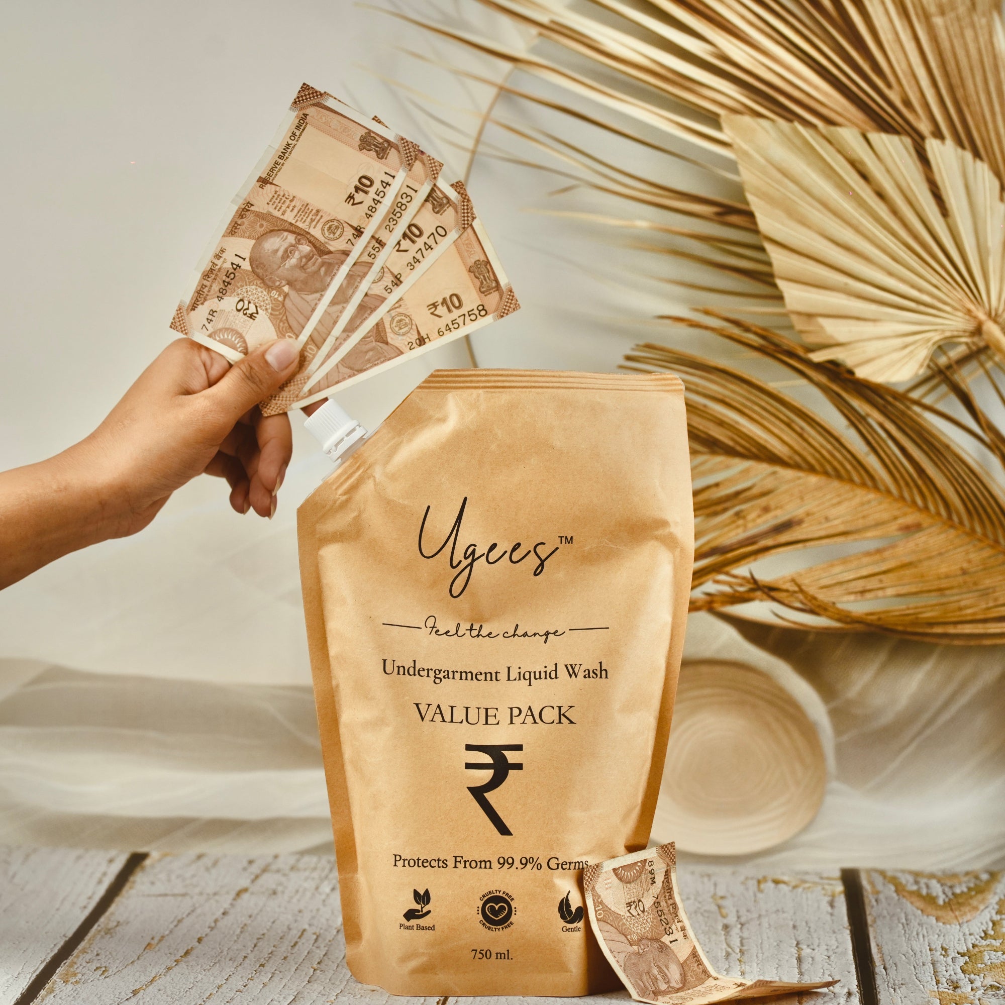 A hand holding Indian currency notes in front of a packet labeled &