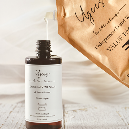 A bottle of Ugees undergarment wash with a refill pack in the background, on a wooden surface.