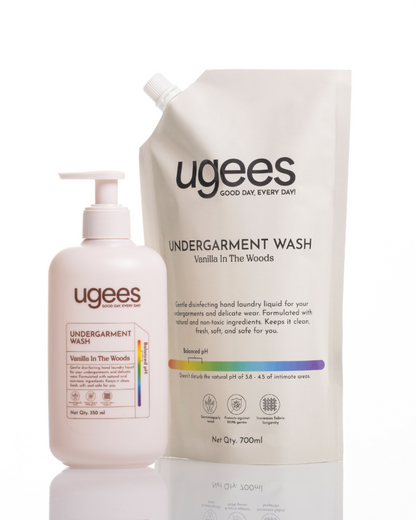 A bottle and a large refill pouch of ugees Undergarment Wash in Vanilla in the Woods, displayed on a reflective white surface against a white background.