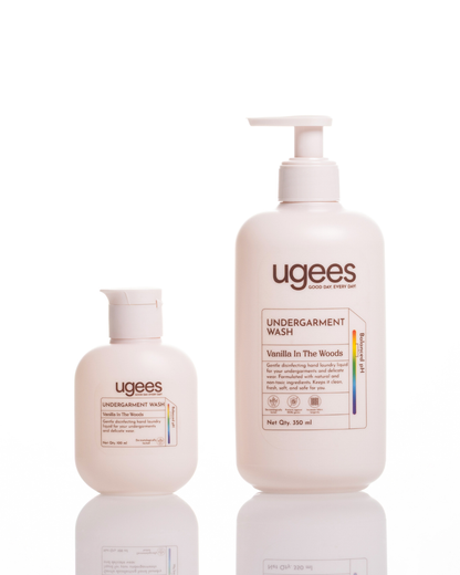 Two Ugees Undergarment Wash bottles on a white reflective background: a smaller pump bottle and a larger squeeze bottle, both in a warm off-white color with brown and black text.